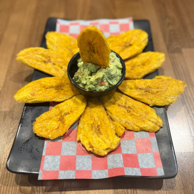 Don Pollo's tostones, fried plantains, arranged around a bowl of guacamole on a black plate.