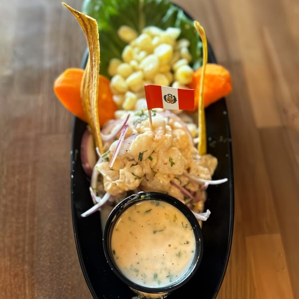 Peruvian ceviche with corn, plantain chips, and a Peruvian flag, served with a side of sauce.