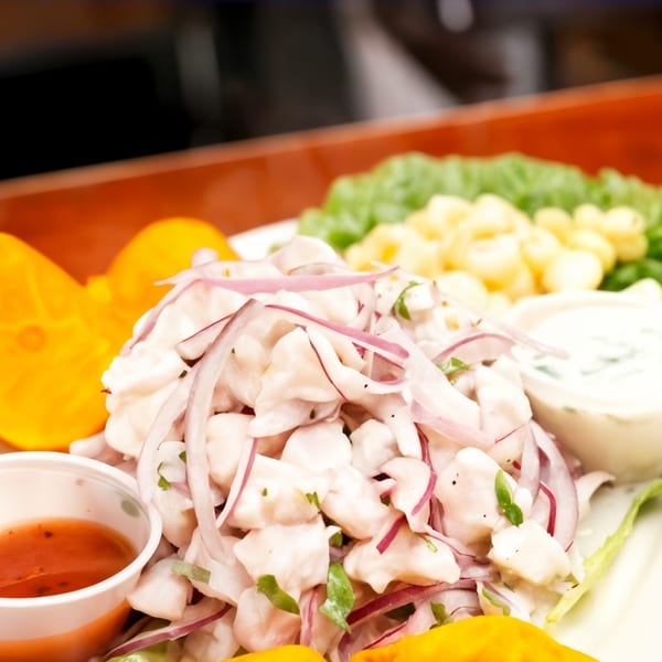 Peruvian ceviche with white fish, red onions, corn, sweet potato, and sauces on a white plate.