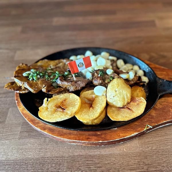 Peruvian anticuchos with potatoes, corn, and a Peruvian flag on a sizzling hot plate.