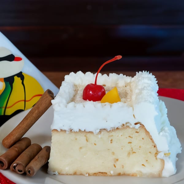 Slice of Peruvian tres leches cake with whipped cream, a cherry, and cinnamon sticks.