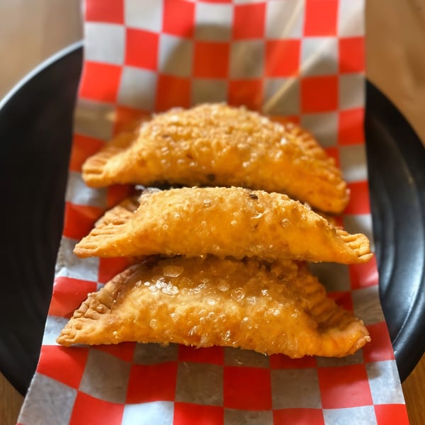 Three golden-brown Peruvian empanadas, sprinkled with sugar, stacked on red and white checkered paper.