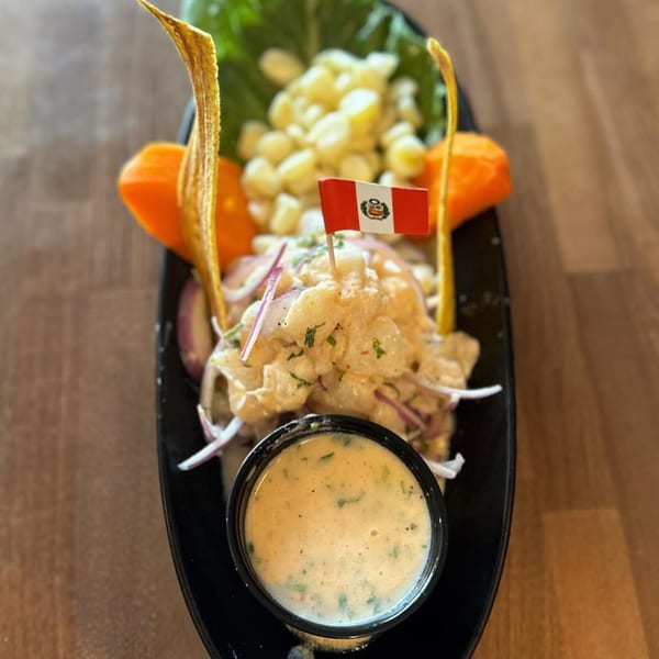 Peruvian ceviche with corn, sweet potato, plantain chips, and a Peruvian flag on a black plate.
