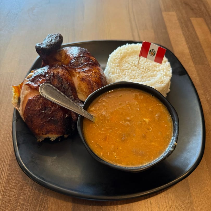 Don Pollo's Peruvian rotisserie chicken with rice, beans, and a Peruvian flag on a black plate.